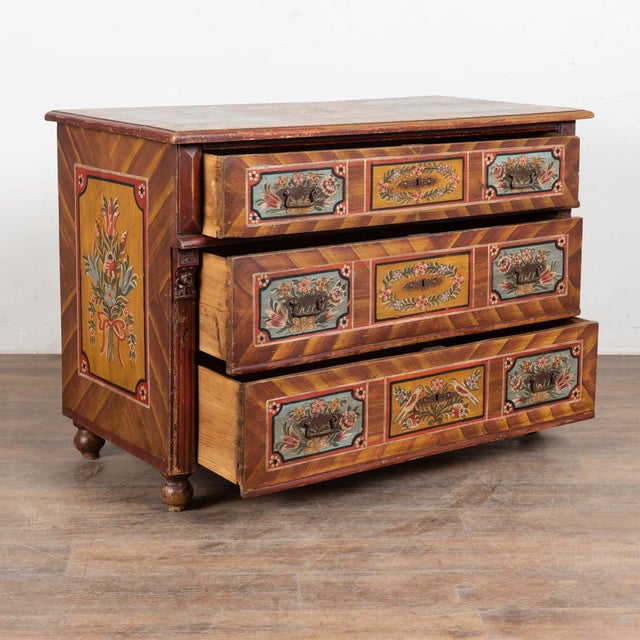The soft earth tone colors are all original on this hand-painted antique chest of three drawers from Hungary. The lovely...