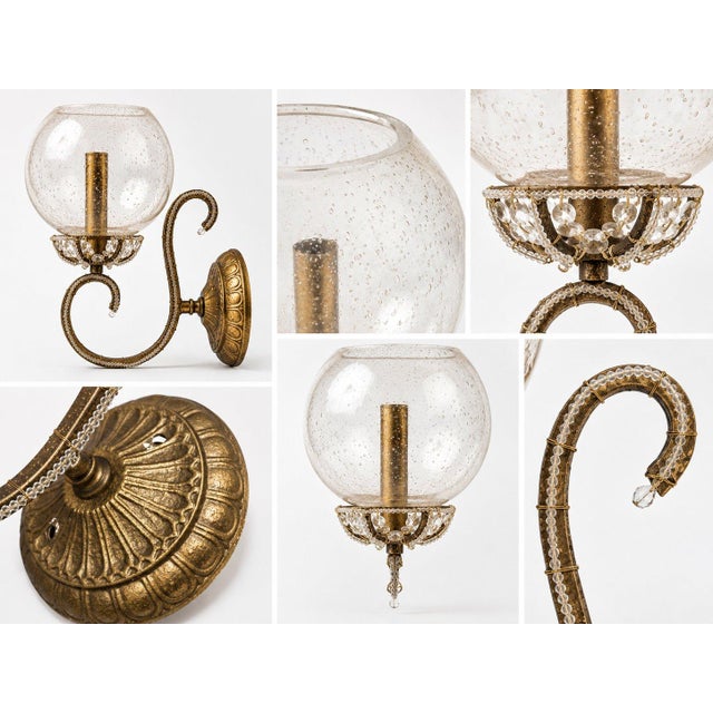 This gold wall sconce features a bubbled glass shade and decorative clear beads wrapped around the metal arm and base,...