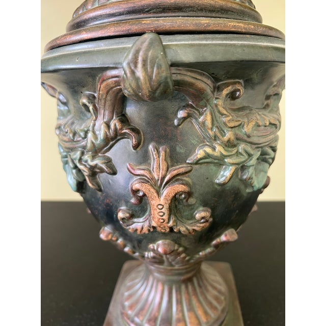 Striking pair of antique-style Neoclassical urns featuring ornate floral and foliate relief, removable lids, and...