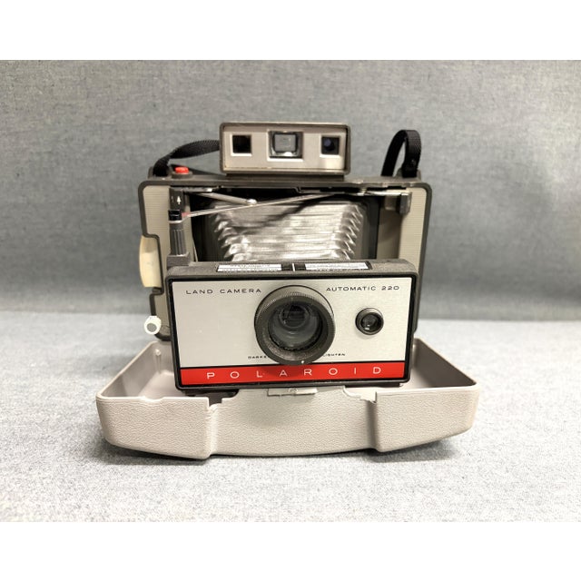 A 1960s Polaroid Land Camera - #220. The vintage camera has folding bellows, a plastic body, two lenses and two windows. A...