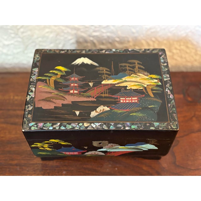 Midcentury black lacquered jewelry box with inlaid mother-of-pearl surround and hand-painted landscapes. Painted mirror on...