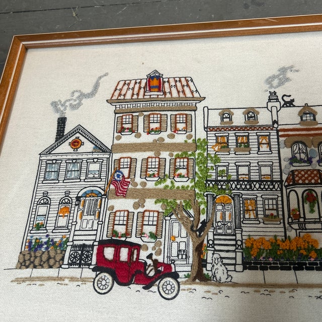 Contemporary 1980’s style embroidery of a downtown with pets and townhomes. Signed on the back. Measures 23x13.5 framed....