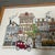Contemporary 1980’s style embroidery of a downtown with pets and townhomes. Signed on the back. Measures 23x13.5 framed....