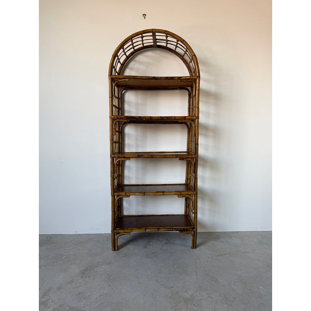 Beautiful 1970's vintage coastal etagere featuring a striking arched bamboo and rattan frame with five wood display...