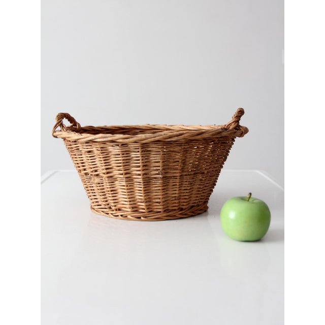 This vintage oval wicker basket features a deep woven body, warm brown finish, and distinctive twisted handles at either...
