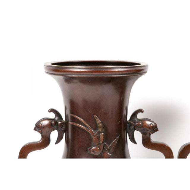 A refined pair of late 19th century Japanese Meiji period bronze vases, each cast with stylized dragon-form handles and a...
