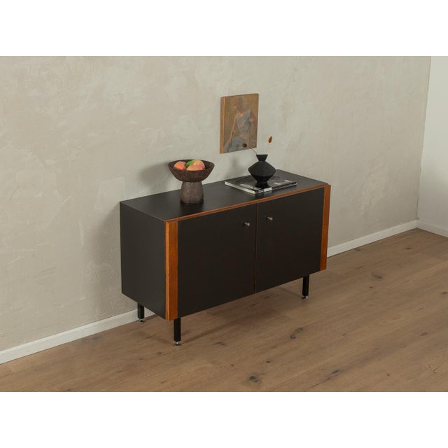 Classic chest of drawers from the 1960s. High-quality body in teak veneer with two doors, a shelf and new square steel...