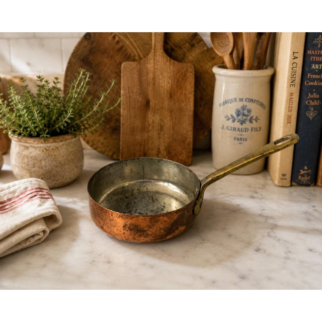 Antique copper butter warmer or small saucepan with a tin-lined interior and riveted brass handle. The piece has a warm...