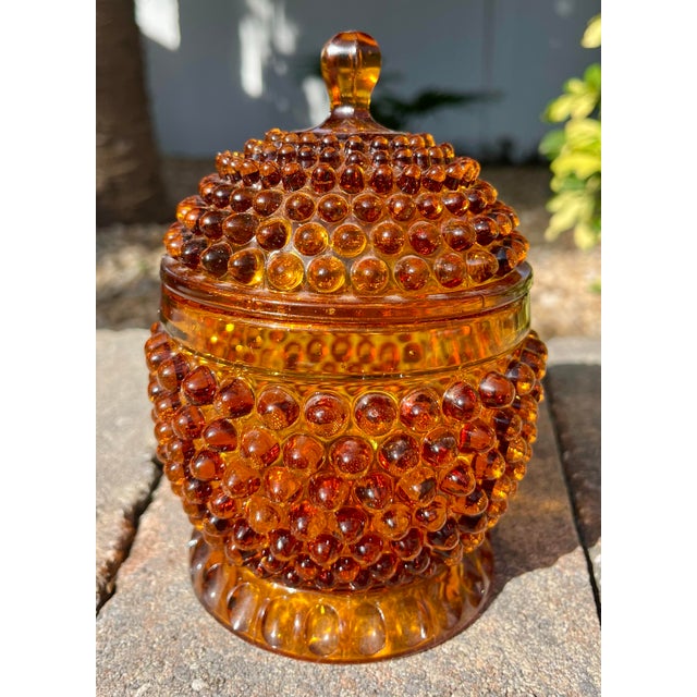 Footed amber art glass lidded candy jar featuring raised hobnail pattern. Lovely vintage piece with a beautiful rich and...