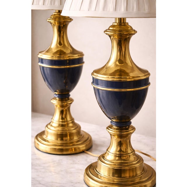A refined pair of vintage Hollywood Regency table lamps crafted in polished brass with deep navy blue accent detailing,...