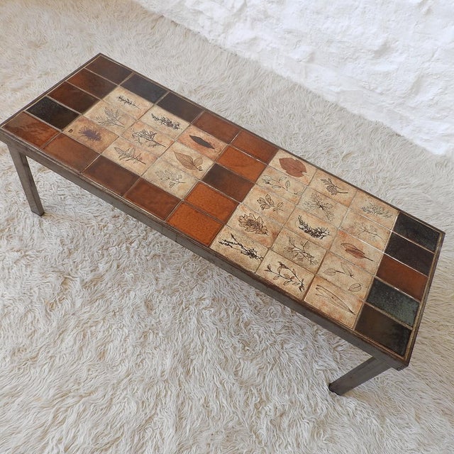 Low rectangular table with a brushed iron frame and a top made of handcrafted tiles, alternating between "Herbier"...