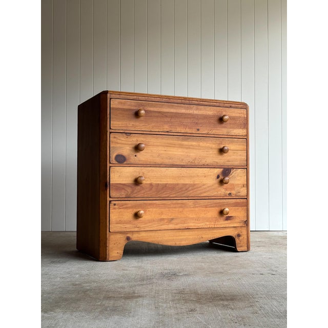 Vintage knotty pine chest with four drawers, rounded fronts, turned wooden knobs, and a shaped apron base. Warm honey-...