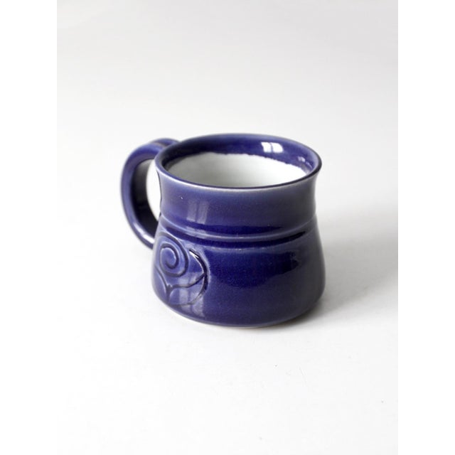This vintage handmade studio pottery mug features a rich indigo glaze with violet undertones and a rounded form adorned...