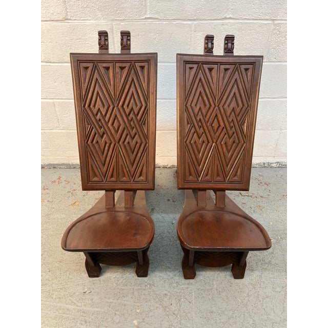 Make a striking design statement with this pair of low-slung carved chairs featuring bold geometric forms and a commanding...