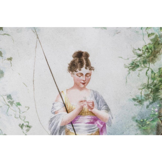 Painted porcelain plate figuring a fisherwoman near a lake in the middle of nature. She holds a fishing rod under her arm...