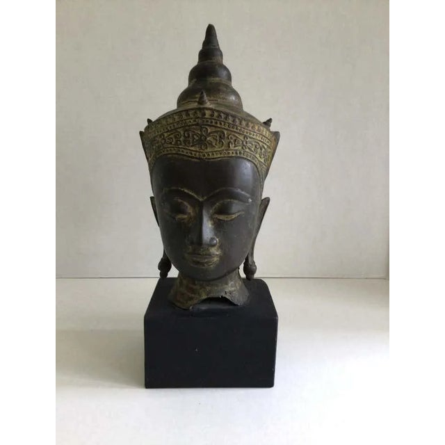 1960s Cast Bronze Crowned Tibetan Buddha Head on Painted Wood Base Face has a meditative expression Half-closed eyes and...