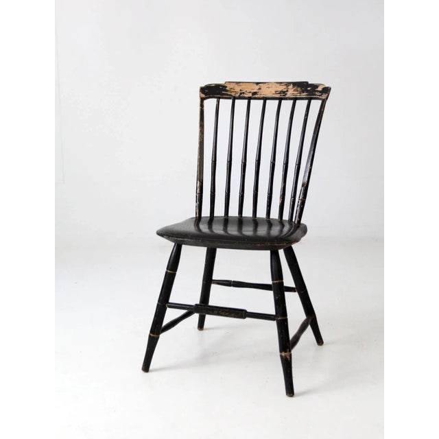 An antique Windsor chair featuring a classic birdcage spindle back and original black-painted finish accented with gold...