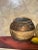 Stunningly arranged still life of wine, clay vessel, and fruit atop a burgundy table cloth. The background of the...