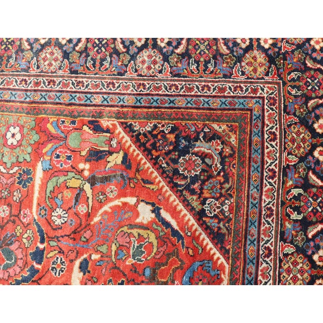 This Antique Rug features a large central diamond design, replete with floral and sub-geometric motifs rendered in...
