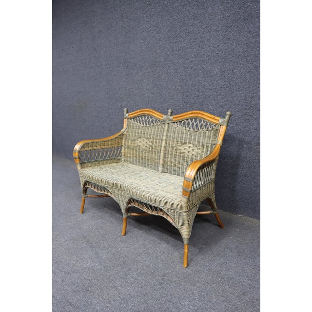 Woven wicker loveseat featuring a warm honey-toned frame, curved arms, and a shaped back with decorative lattice details....