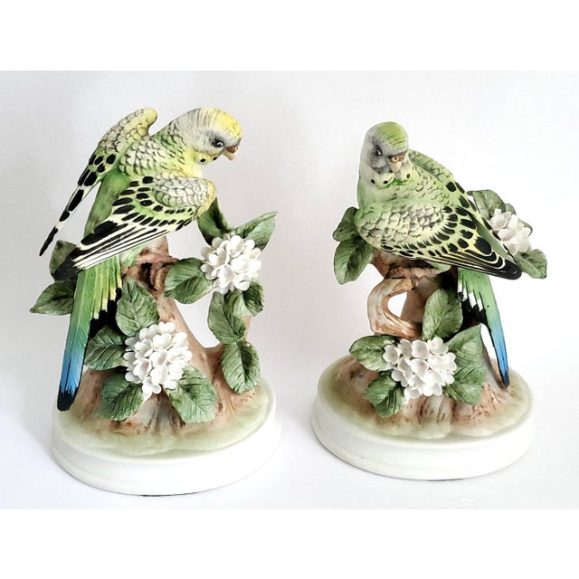 Offering a pair of hand painted porcelain parakeet figurine sculptures, circa 1960s. These ceramic figurines depict two...