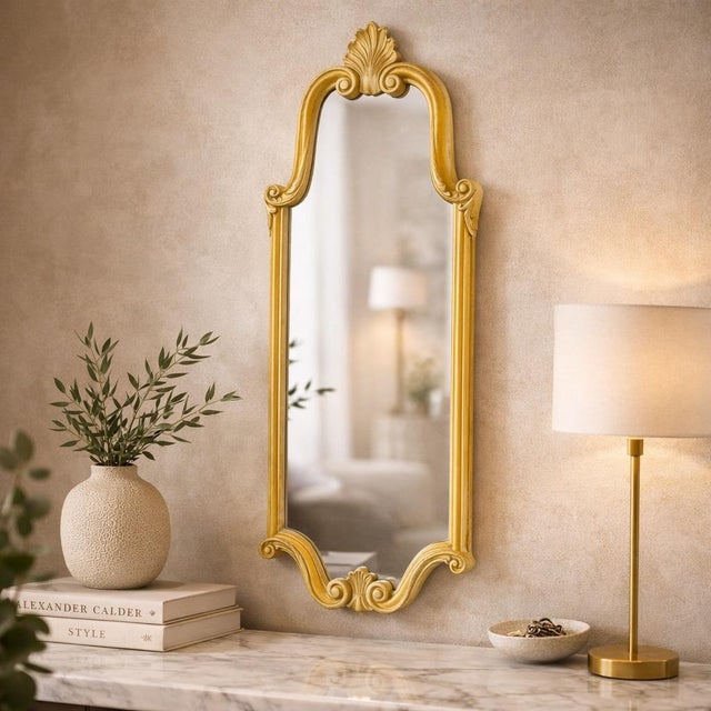 An elegant and highly decorative vintage wall mirror dating to the 1940s, crafted in carved wood with a warm gilt finish...