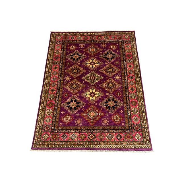 This naturally dyed wool Kazak rug has a rich purple field filled with rows of stepped medallions. Ivory, navy, gold, and...