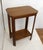 A small, two-tiered side table (pedestal table) in the Art Deco style, with a top shelf featuring chamfered corners and a...