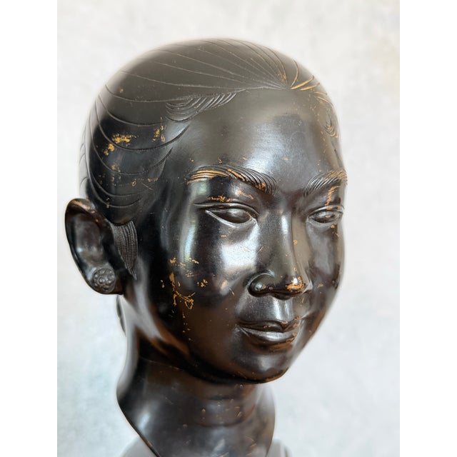 Pair of patinated bronze bust sculptures depicting young Vietnamese women, each mounted on a black-painted wooden plinth...