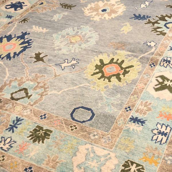 A beautifully Turkish Oushak rug featuring a soft gray field framed by a turquoise border, accented with large-scale...