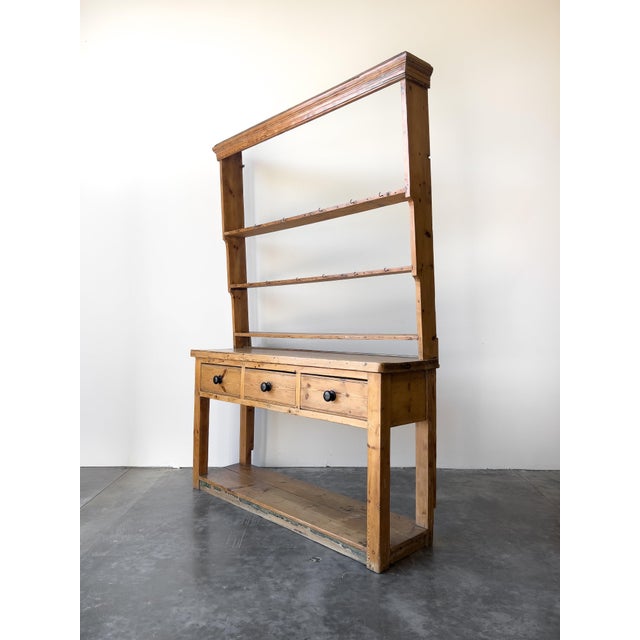An antique Georgian pine pot board with an open plate rack above. Three drawers with black knobs and a full length lower...