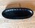 An elongated black wood tray featuring a distinctive hammered-style texture and streamlined oval form. The matte finish...