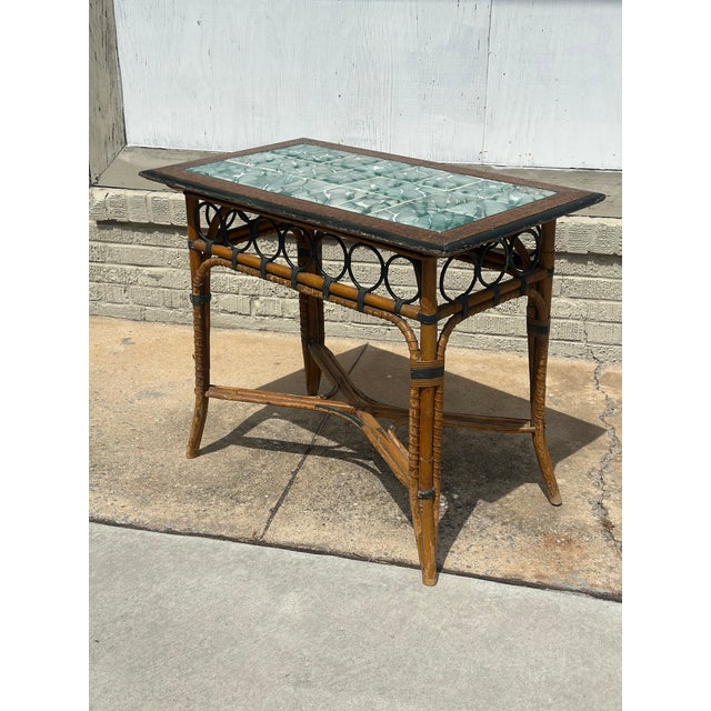 An elegant antique tile-top accent table featuring a richly detailed bamboo frame with decorative black metal ring accents...