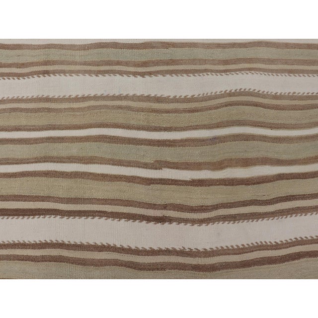 Handwoven in 1956, this vintage Persian Kilim rug is a masterclass in minimalist design and tribal craftsmanship....