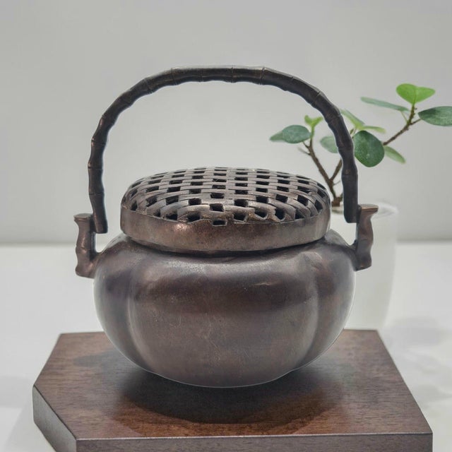 A finely cast Chinese bronze incense burner of portable hand censer form, featuring a domed pierced lattice cover and...