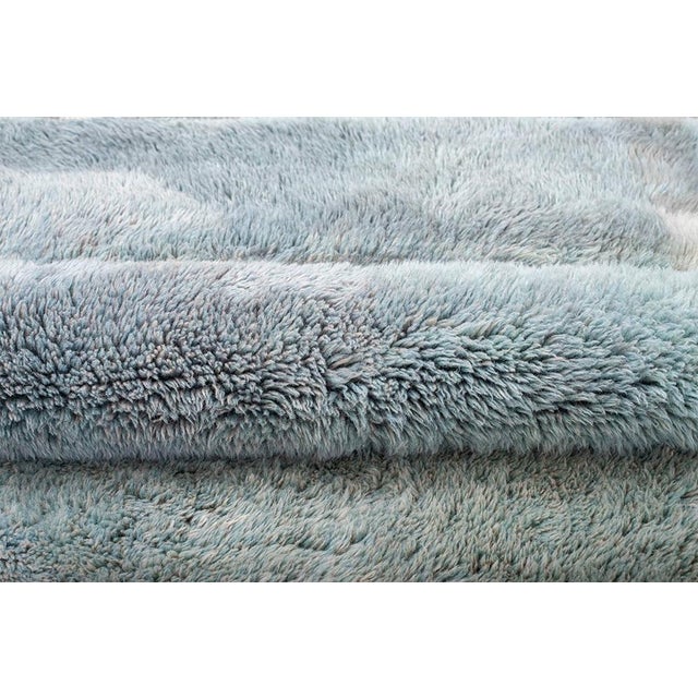 A quietly textured rug in soft oatmeal and grey-blue tones, its surface broken into gentle horizontal bands with fringe...