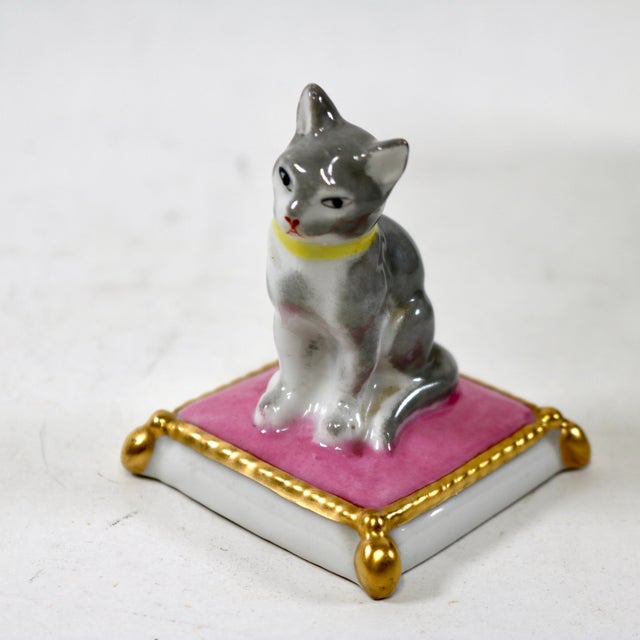 A stunning gray and white cat with yellow collar sitting regally atop a gold border and tasseled pink pillow figurine....
