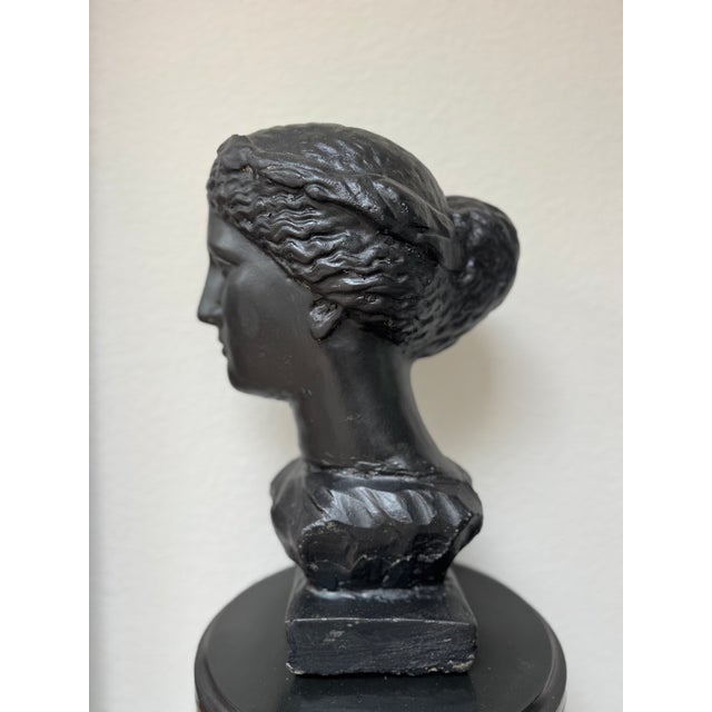 A substantial Neoclassical female bust cast in solid concrete and finished in black. The sculpture depicts an idealized...