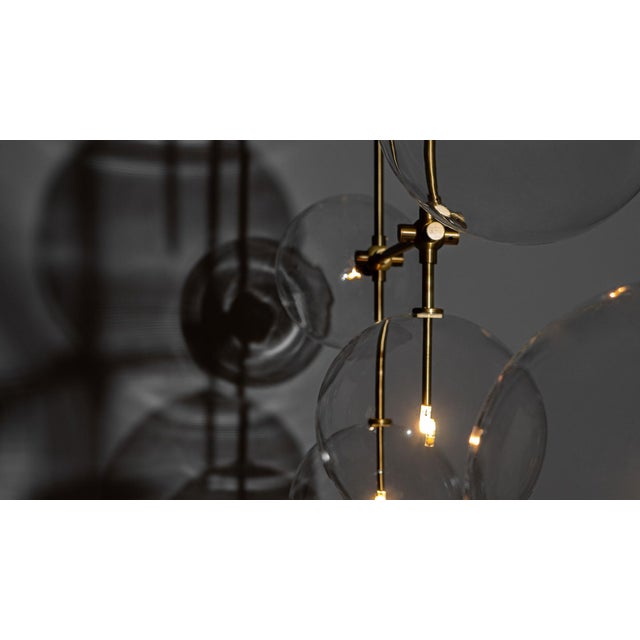 An array of ethereal glass globes floats weightlessly around a right-angled geometric lattice. The mouth-blown spheres are...