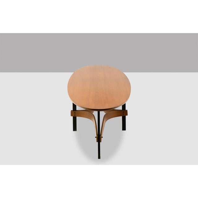 Guglielmo Ulrich. Light teak coffee table. Elongated oval tabletop supported by four black-lacquered metal legs and teak...