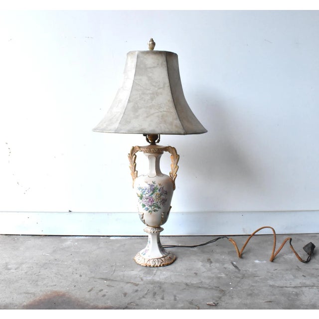 An antique ceramic urn lamp, early 20th-century, with floral relief decoration, gilt details, and the original stretched...