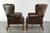 This unique set of two large, characterful English-style cowhide wingback chairs features a beautiful dark cognac color...