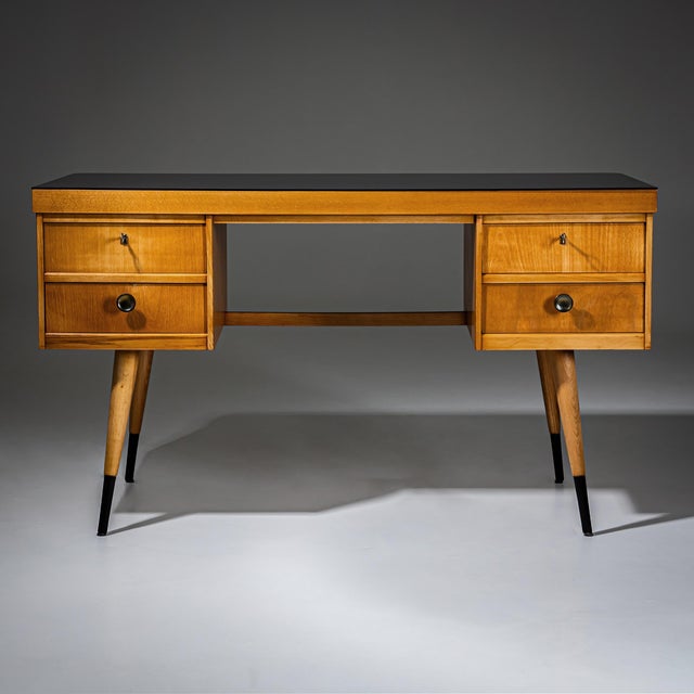 Low desk crafted in light beechwood, standing on tapered legs with black ribbed feet. The desk offers ample storage with...