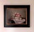 This oil on panel artwork features a delicate still life arrangement centered around a silver-rimmed bowl filled with an...