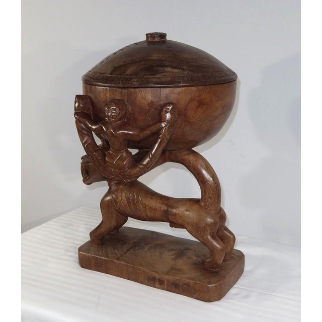 Large pot with a lid consisting of a base formed by a ferocious dog with a slender body supporting the container. A bird...