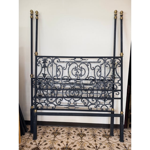 A striking iron canopy bed featuring beautifully detailed scrolling on both the headboard and footboard, accented with...