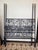 A striking iron canopy bed featuring beautifully detailed scrolling on both the headboard and footboard, accented with...