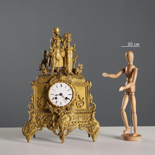 Gilded bronze mantel clock decorated with plant motifs and floral garlands, surmounted by a courtesan with a dove....