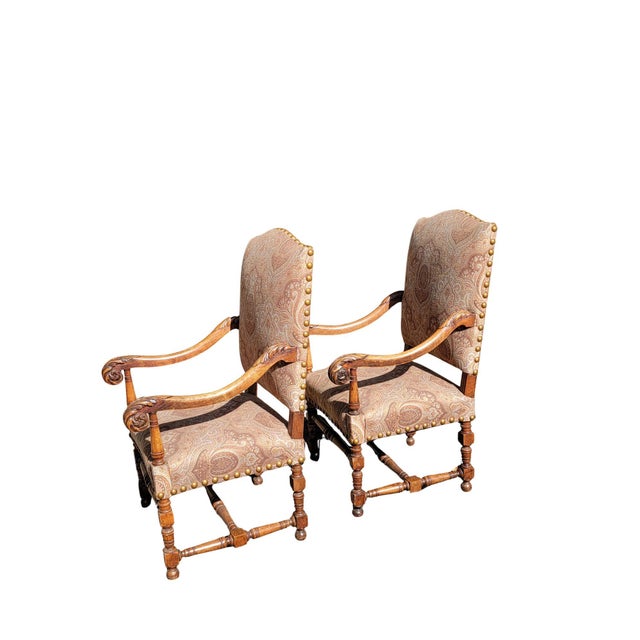 A pair of French Walnut open armchairs with carved Acanthus leaves on the arms on turned legs and stretchers.