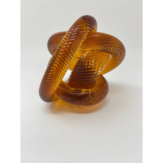 A striking signed amber and cognac art glass infinity knot sculpture, distinguished by its complex interlocking form and...